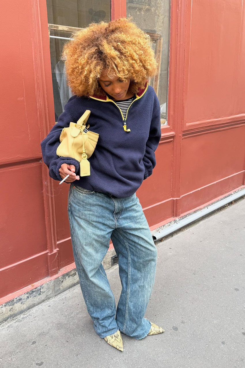 A woman wearing a navy quarter zip jacket, blue jeans, and snakeskin heels