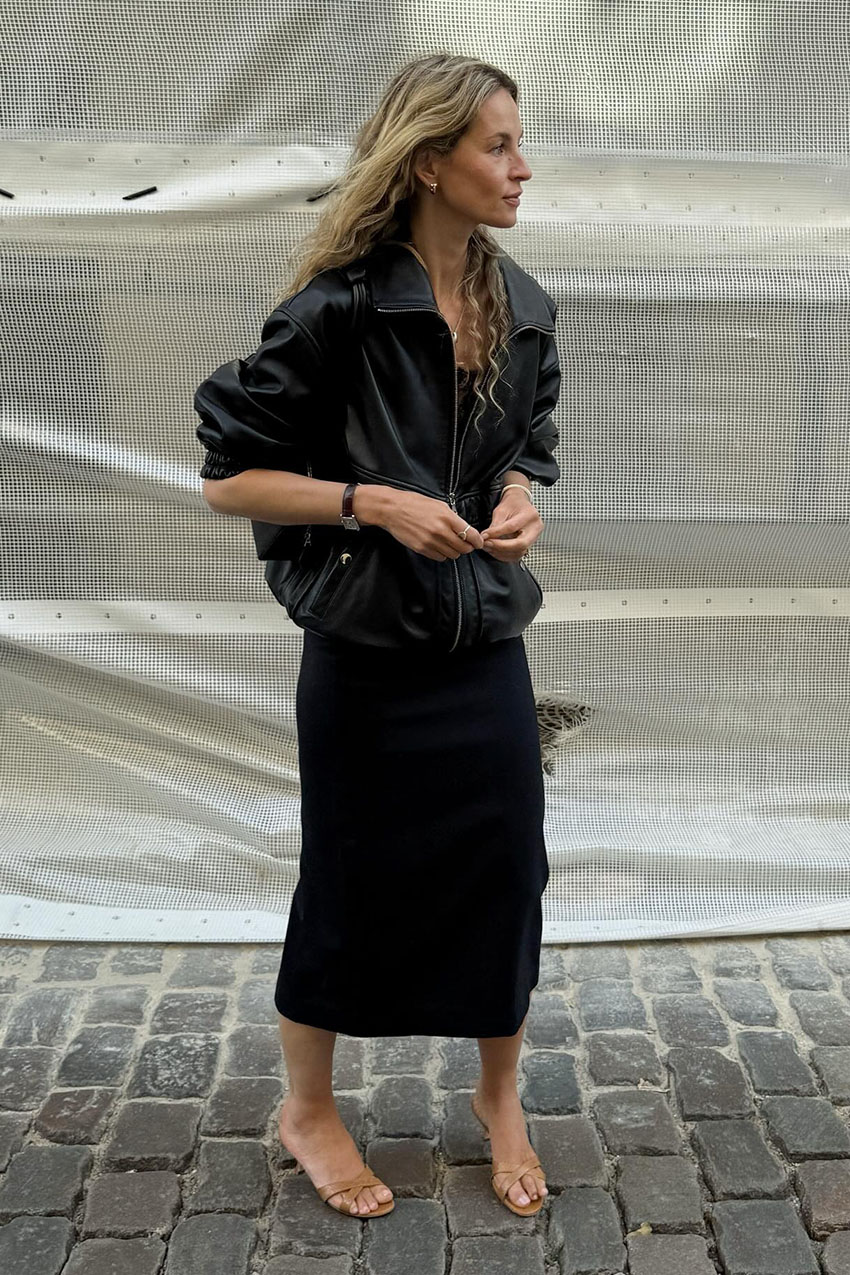 A woman wearing a black leather jacket and black dress with tan sandals