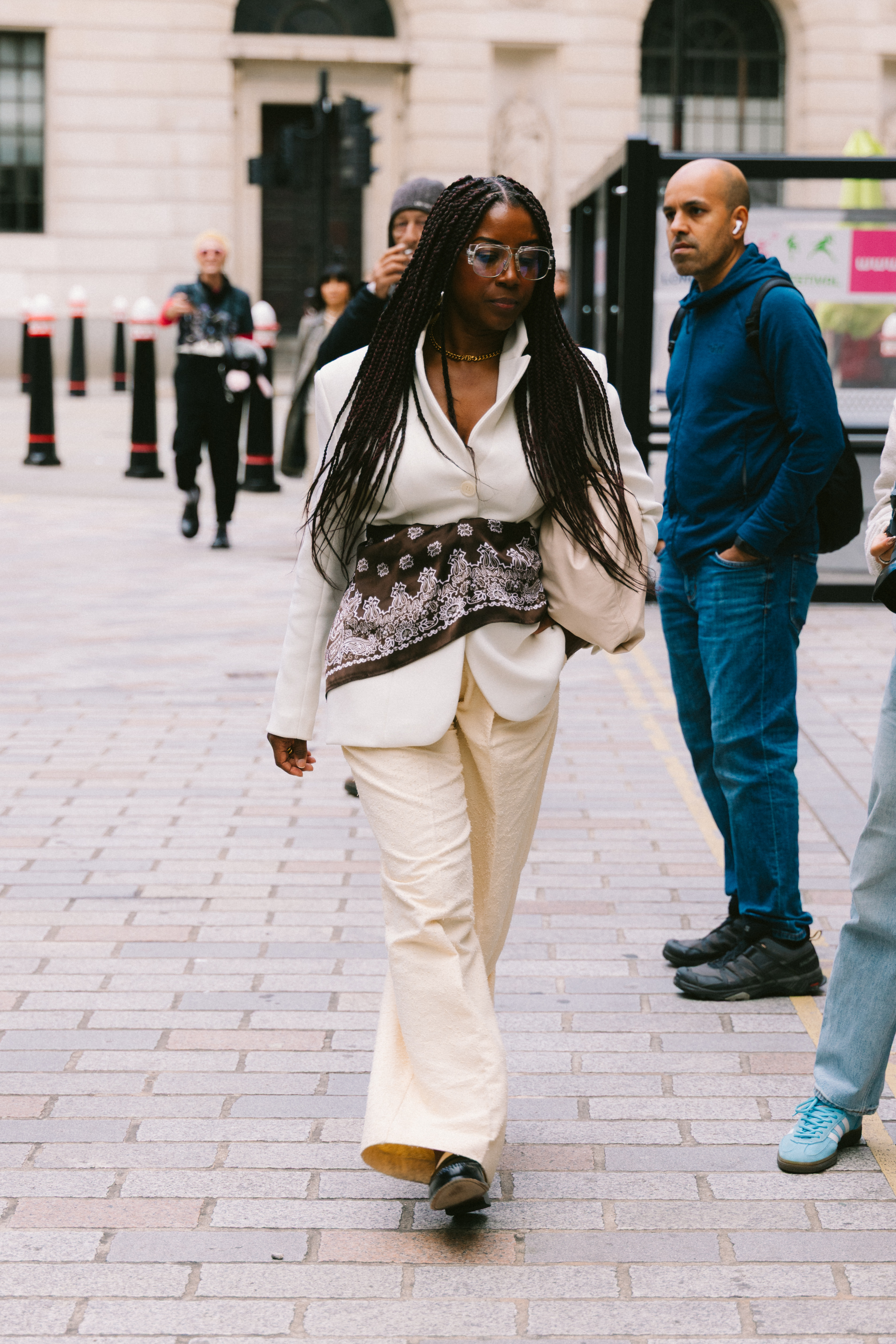 A woman wearing a white blazer, white pants, and a brown scarf