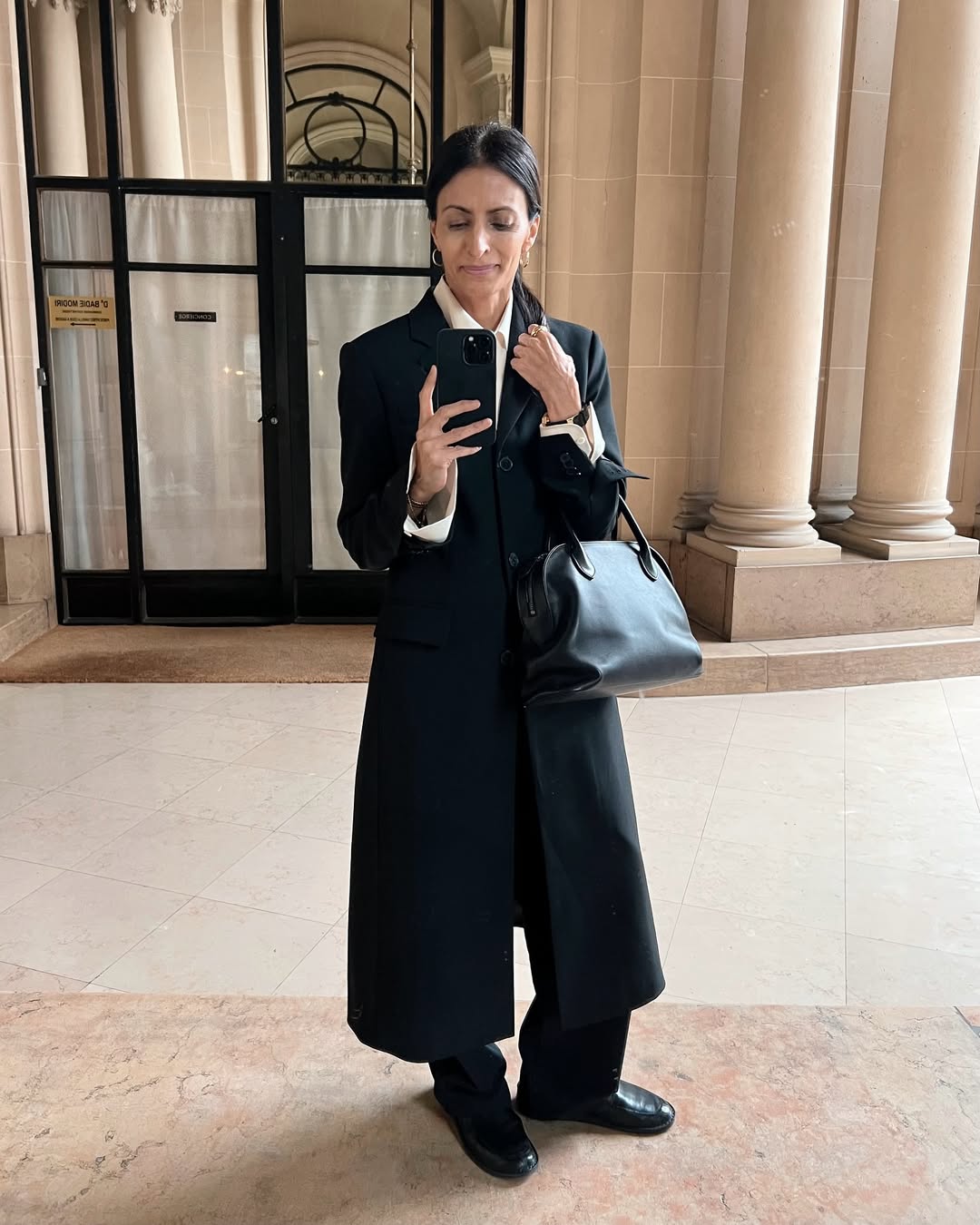 Influencer outfit featuring a black maxi coat, white shirt, bowler bag, and loafers