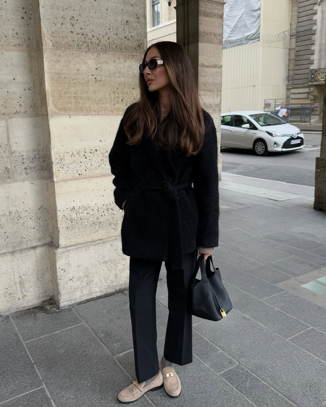 Influencer Felicia Akerstrom wears a pair of beige suede loafers, black slacks, coat, and sunglasses.