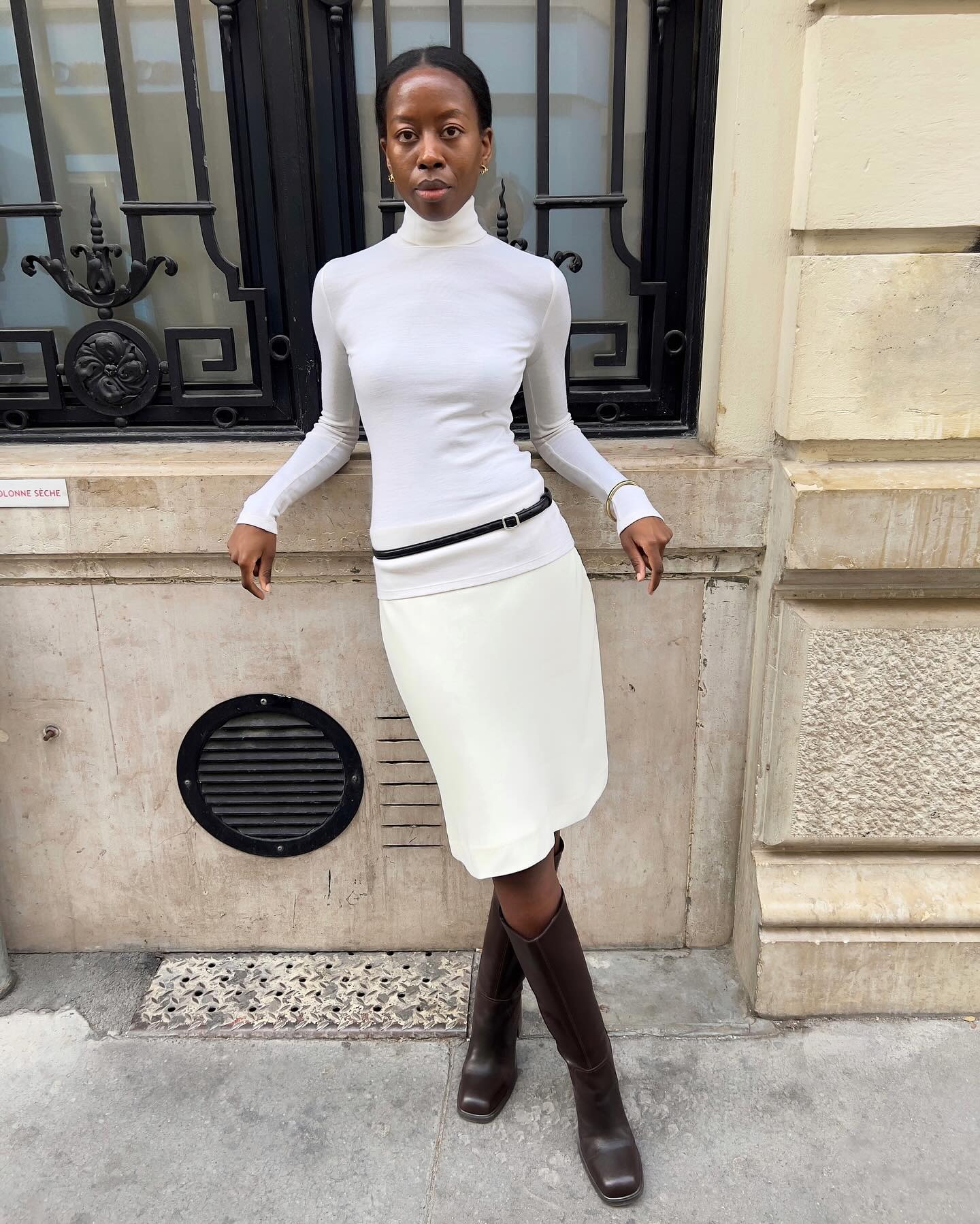 Sylvie wears a white turtleneck, white skirt, and brown knee-high boots.