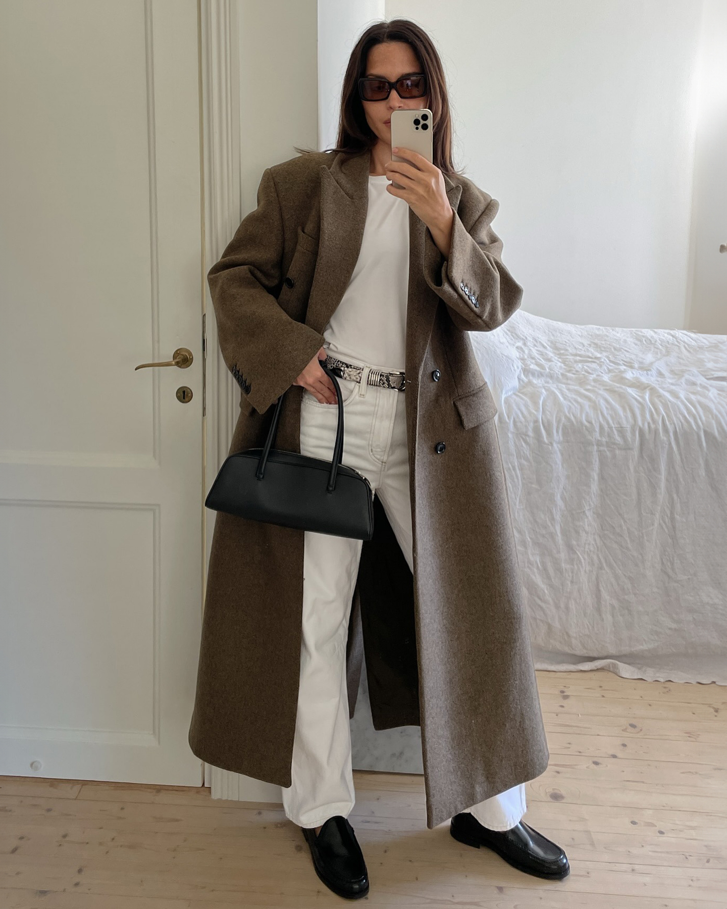 European style influencer Johanna Piispa a wearing chic fall outfit with white jeans, a white T-shirt, snakeskin belt, black East West bag, and black loafers