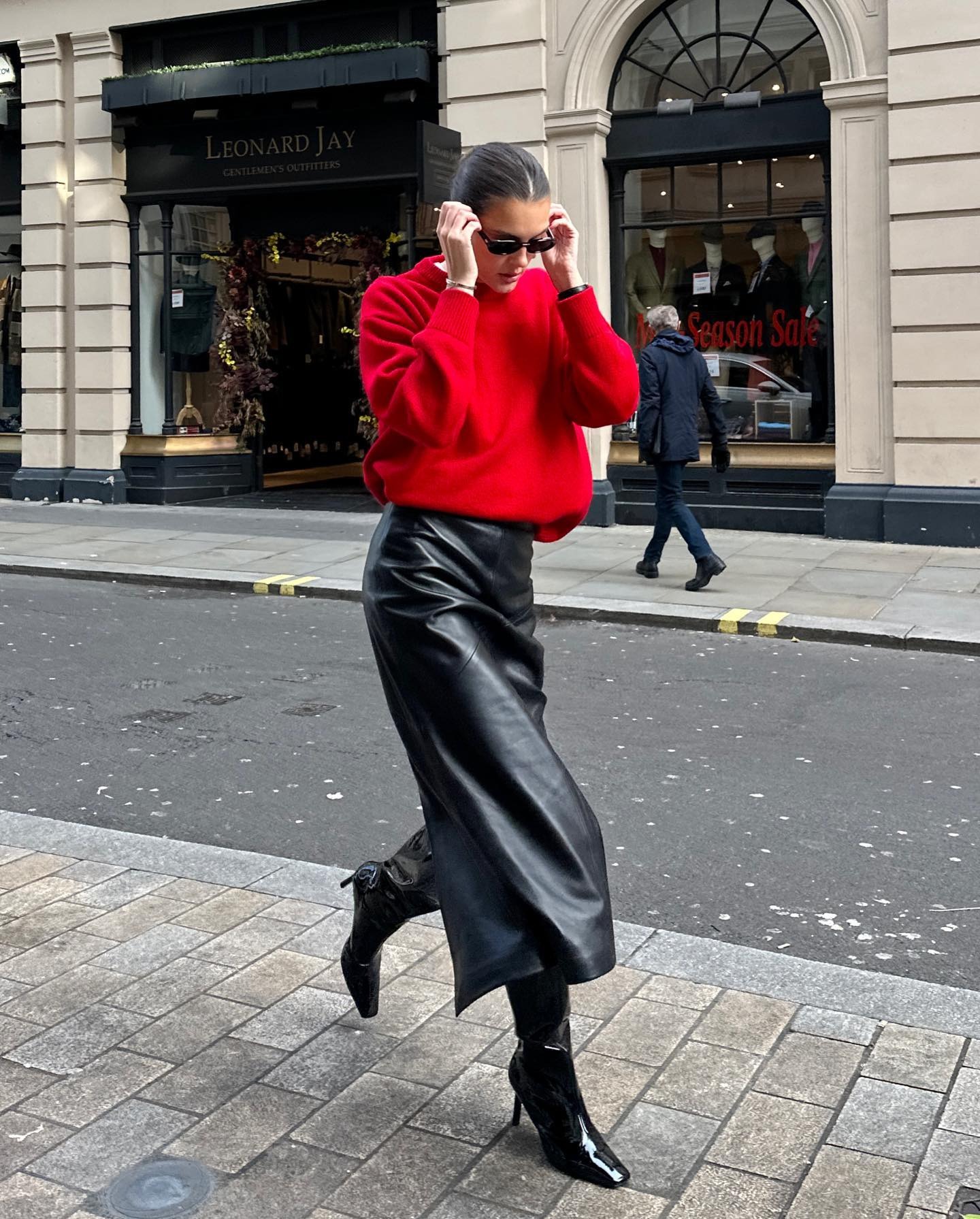A woman wears a red sweater, black pencil skirt, and black knee-high boots.