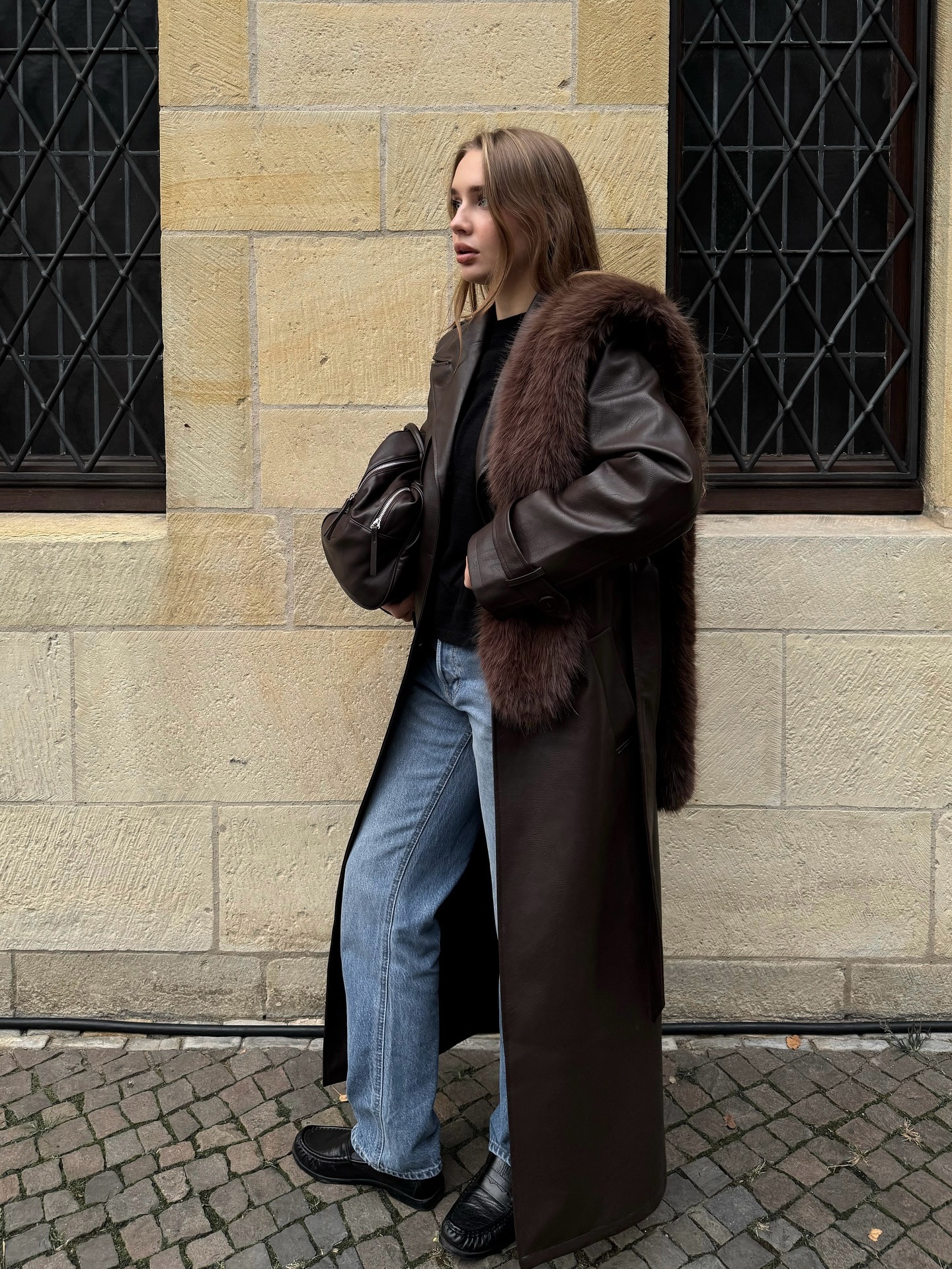 A woman wears a faux fur scarf with a coat and pants.