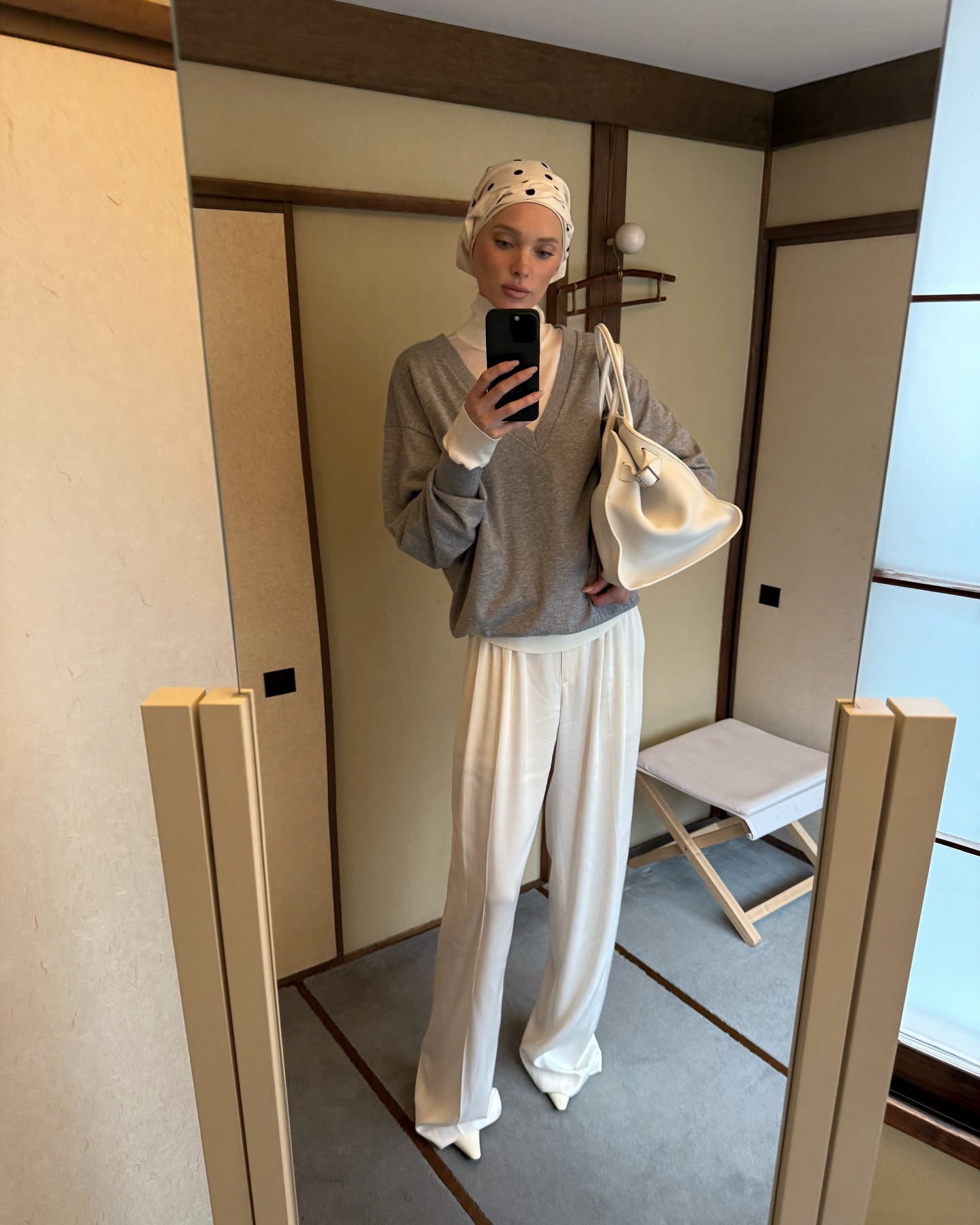 Elsa Hosk wearing a cream turtleneck under a gray V-neck sweater with white pants in Japan.