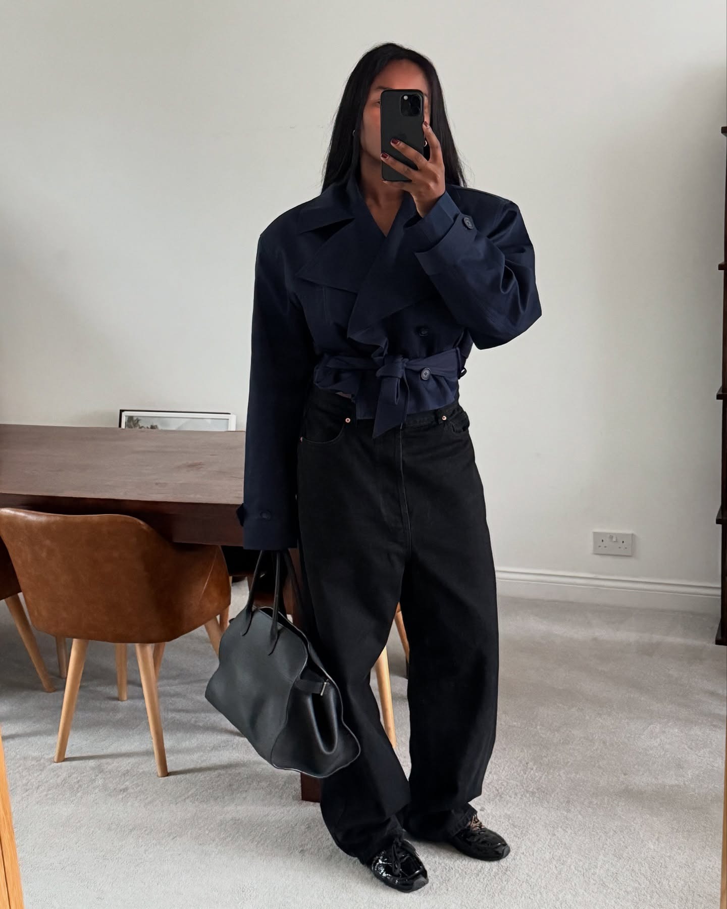 @nlmarilyn wearing a navy-blue cropped trench coat with black jeans, black loafers, and a black The Row Margaux bag.