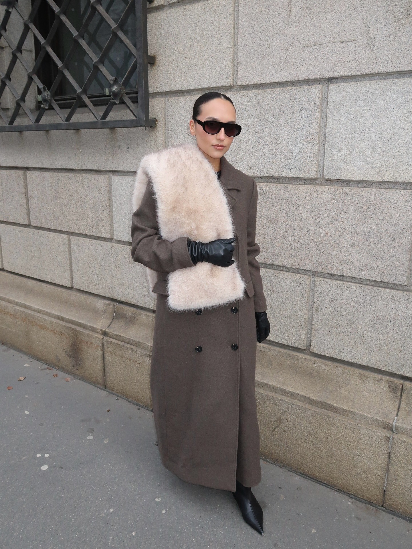 A woman wears a faux fur scarf with a coat and pants.