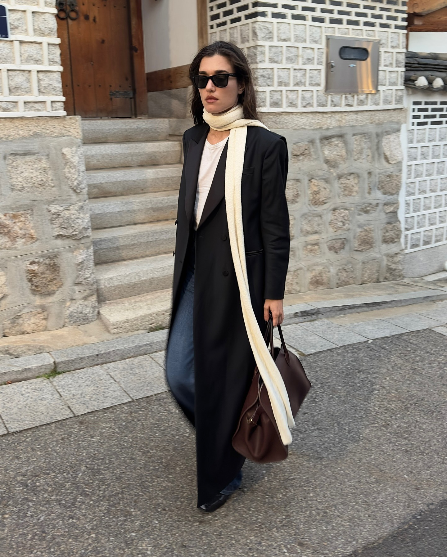Influencer Ilirida Krasniqi wears blue jeans, a white tank, a long black blazer coat, and skinny scarf.