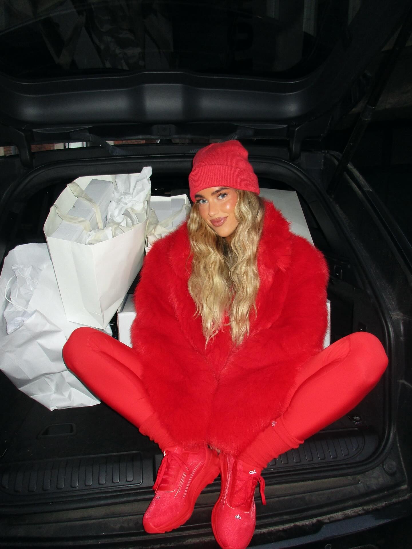 Emili wears a red hat, red fur coat, red leggings, and red alo sneakers.