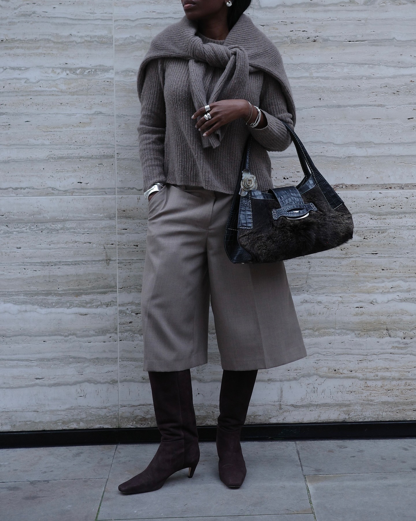 Influencer Danielle Oreoluwa wears a stone colored ensemble with long shorts, a scarf sweater, and suede knee-high boots.