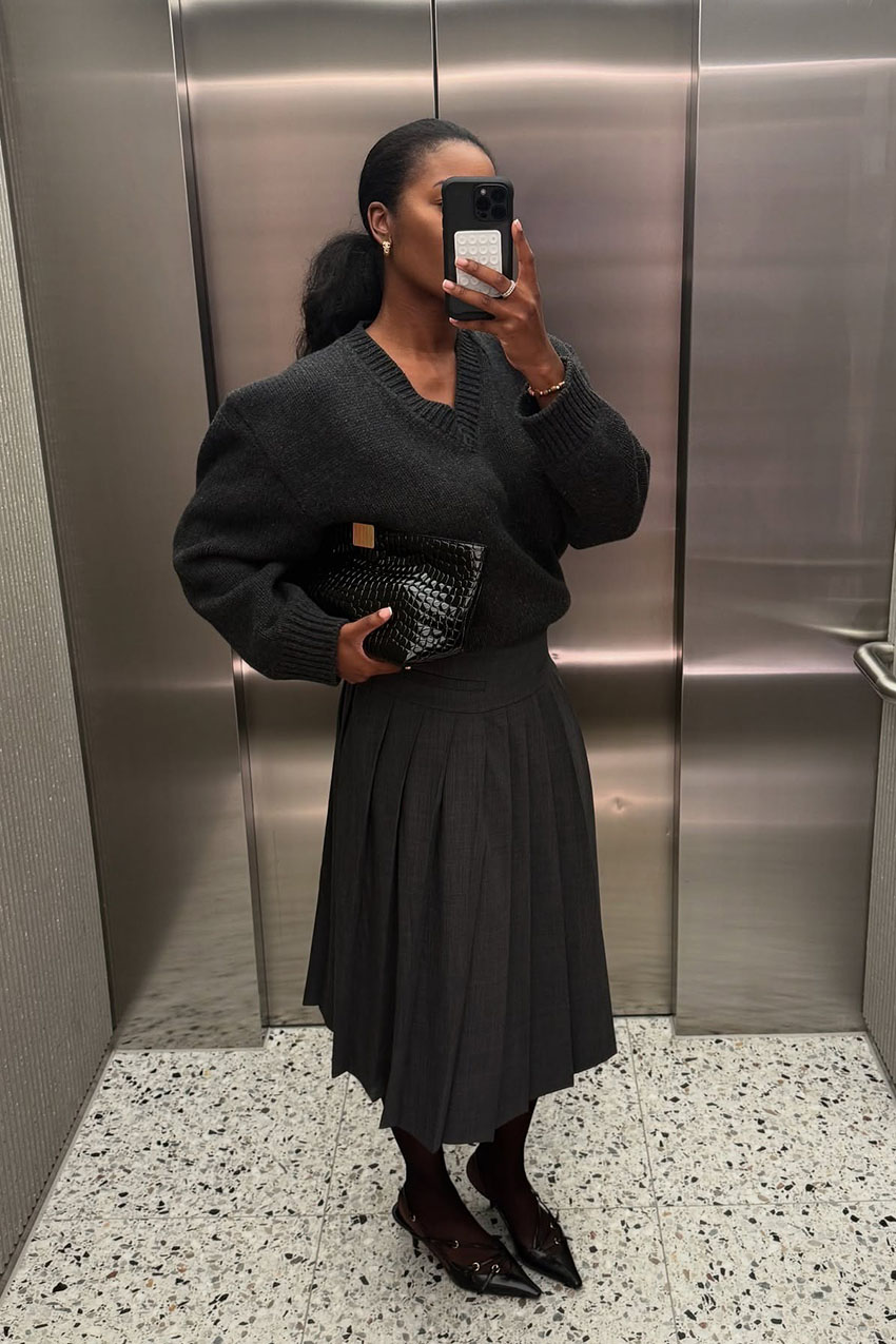 a woman wearing a gray sweater and pleated skirt