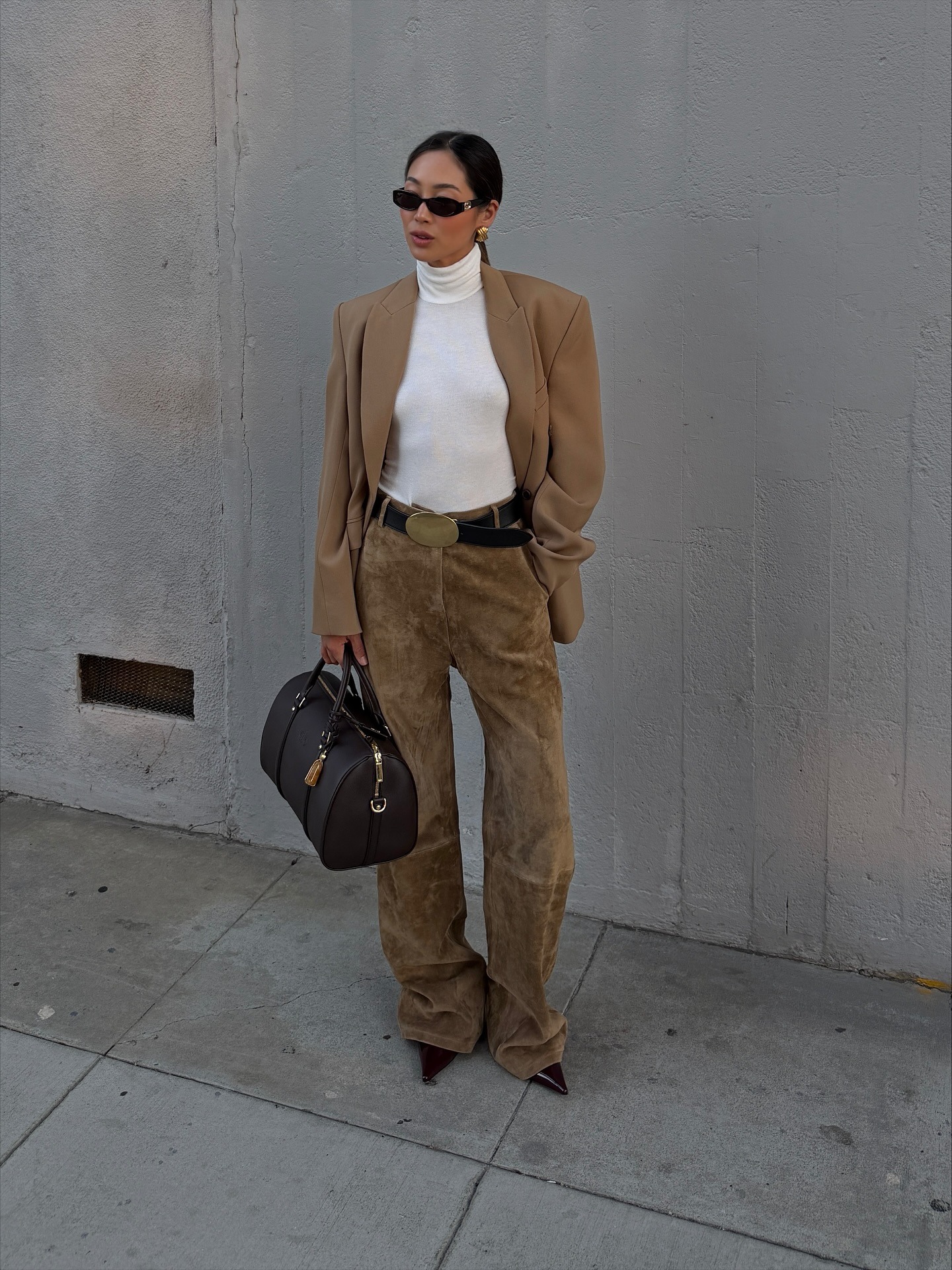 Influencer Aimee Song wears suede pants, a white turtleneck, a beige blazer, pointed-toe heels, an Alo bag, and a leather belt.