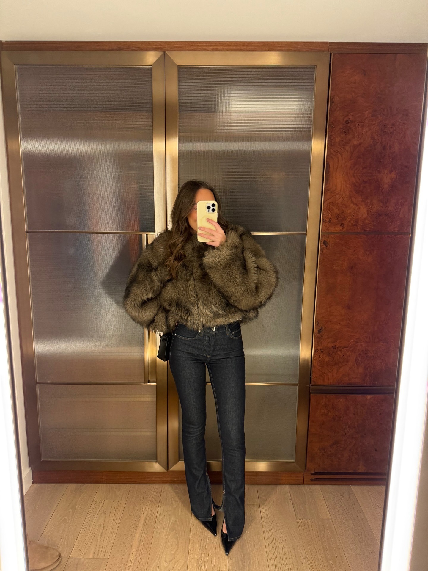 Emma wears a short faux fur coat, dark wash jeans, and black pumps.
