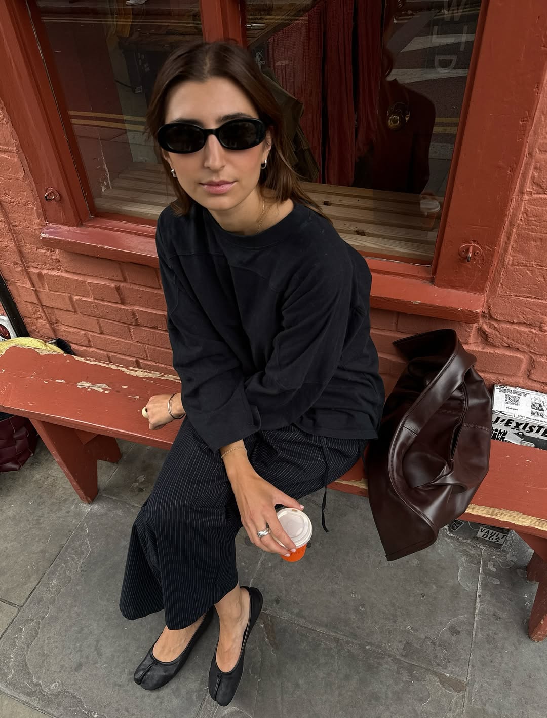 A woman wears a black shirt and pants with a tote bag and ballet flats.