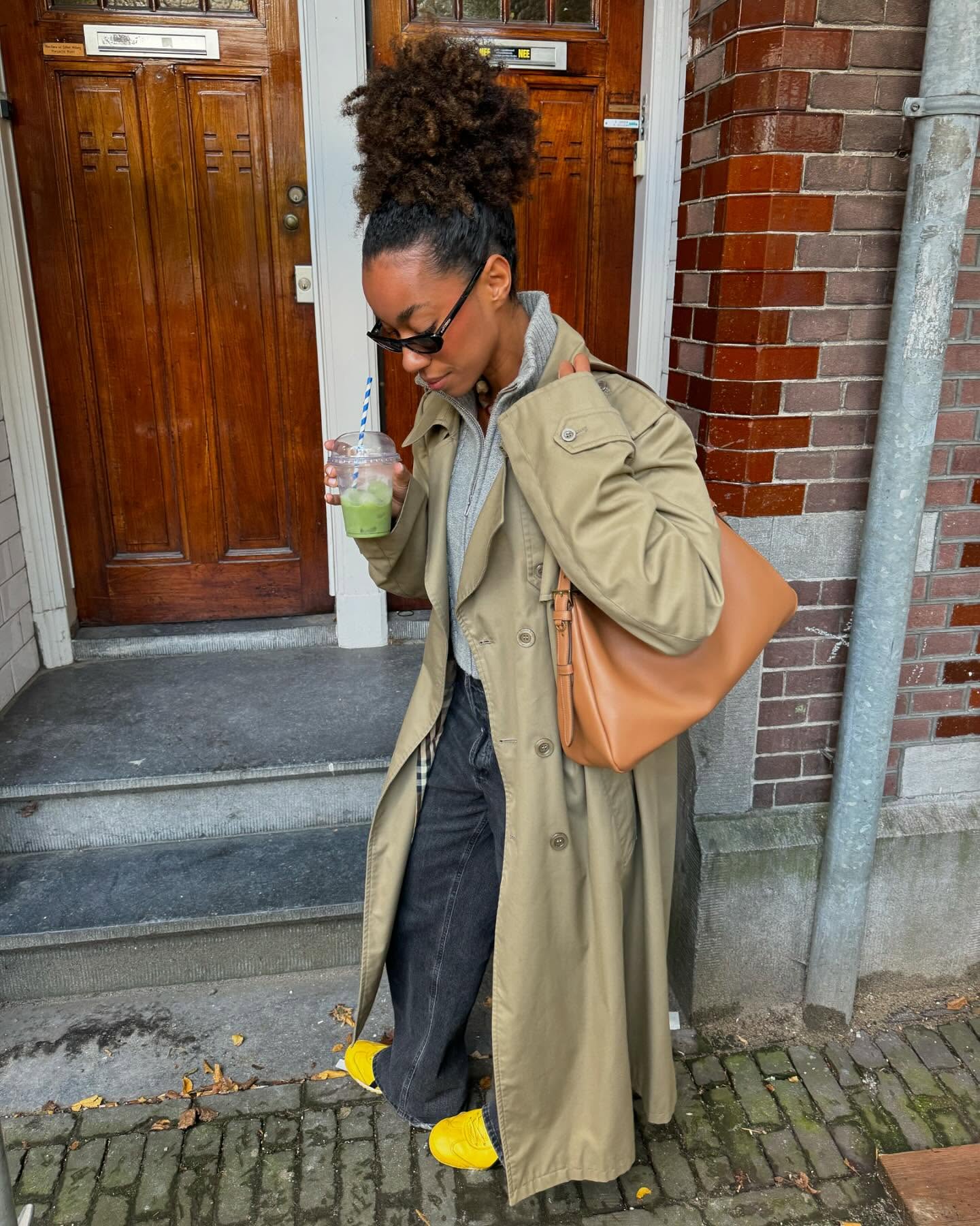 Woman wearing a trench coat, jeans, and sneakers.