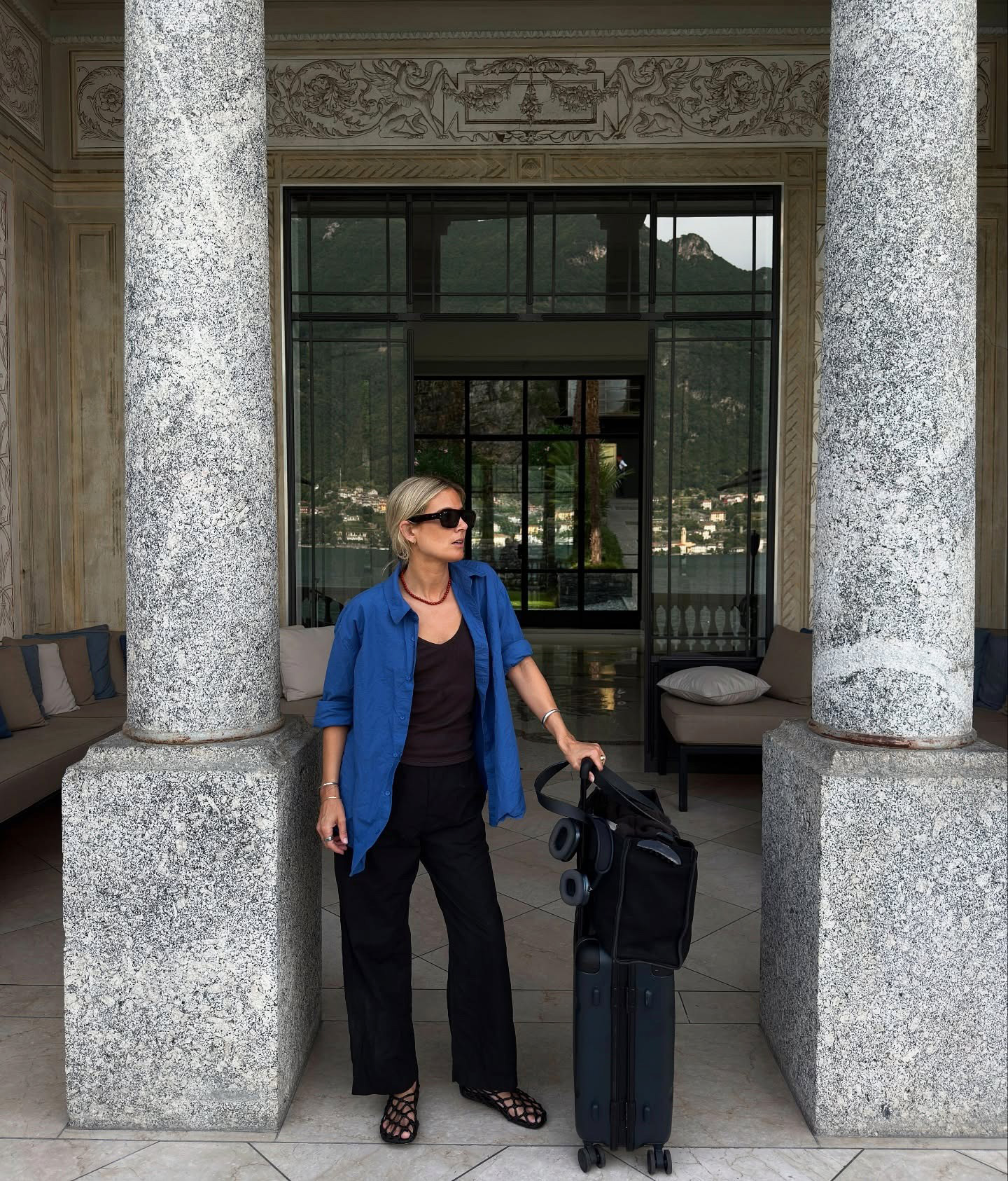 Influencer wearing a button-down shirt and black pants, posing with suitcases